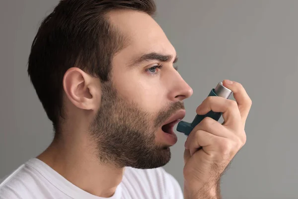吸入器の喘息攻撃は灰色の背景を持つ若い男 — ストック写真