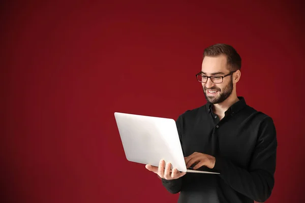 Young businessman with laptop on color background