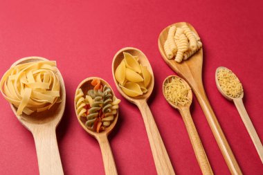 Kaşık ile renk arka plan üzerinde pişmemiş makarna çeşitleri