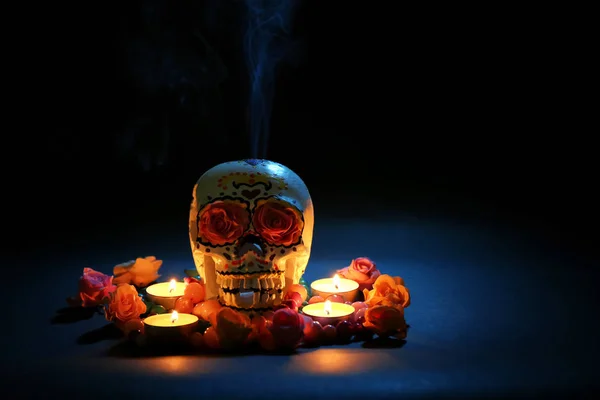 Painted human skull with burning candles and flowers for Mexico\'s Day of the Dead on dark background