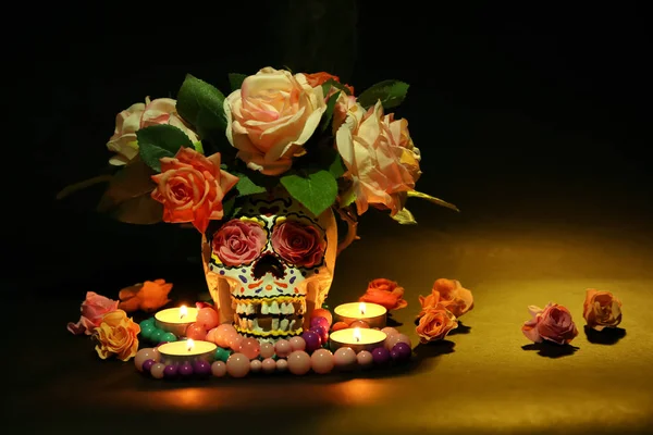 Painted human skull with burning candles and flowers for Mexico\'s Day of the Dead on dark background