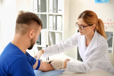 Female doctor drawing a blood sample of male patient in clinic clipart