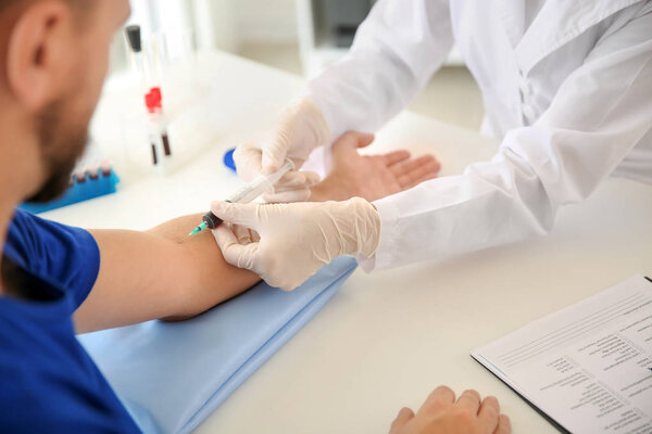 Female doctor drawing a blood sample of male patient in clinic