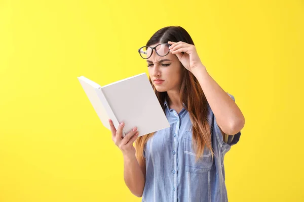 Woman with bad sight trying to read book on color background