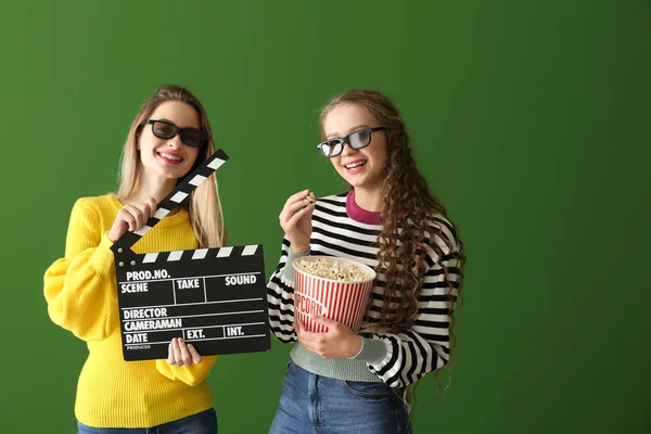 Young women with popcorn and movie clapper on color background