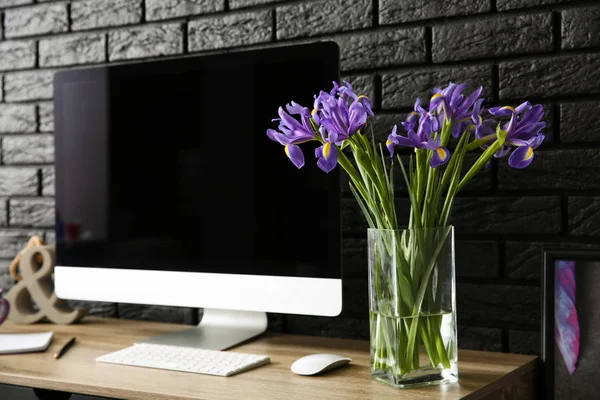 Modern computer and vase with flowers on table