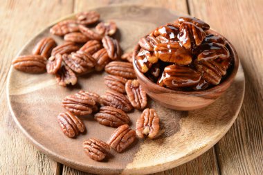 Bowl and plate with tasty pecan nuts on wooden table