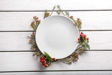 Clean empty plate and floral decor on white wooden background