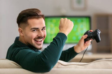Happy young man after winning video game at home