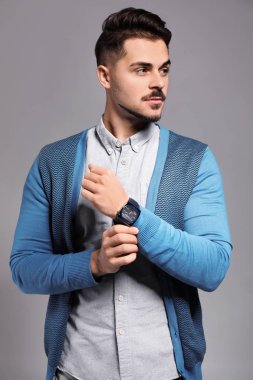 Handsome young man with watch on grey background
