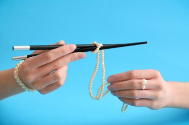 Hands of beautiful young woman with chopsticks and stylish bijouterie on color background