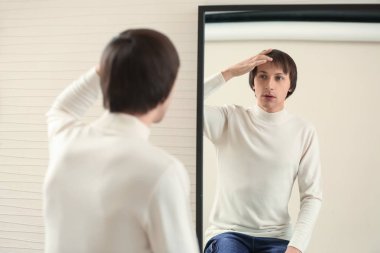 Young transgender man looking on his reflection in mirror