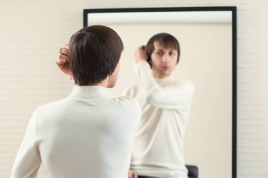 Young transgender man looking on his reflection in mirror
