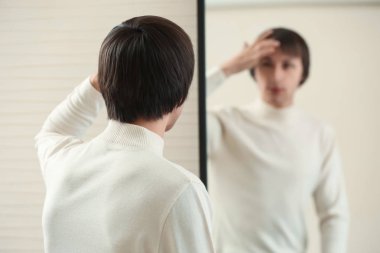 Young transgender man looking on his reflection in mirror