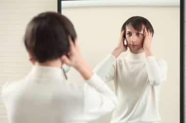 Young transgender man looking on his reflection in mirror