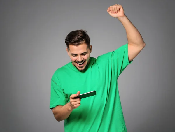 Happy young man after winning game on smartphone against grey background
