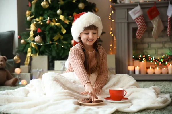 ホット チョコレートを飲み クリスマスイブに家でクッキーを食べてサンタ帽子でかわいい女の子 — ストック写真