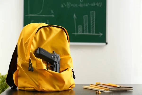 教室のテーブルの上のピストルとバックパックします 学校で銃 — ストック写真