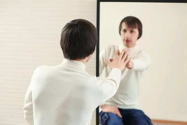 Young transgender man looking on his reflection in mirror