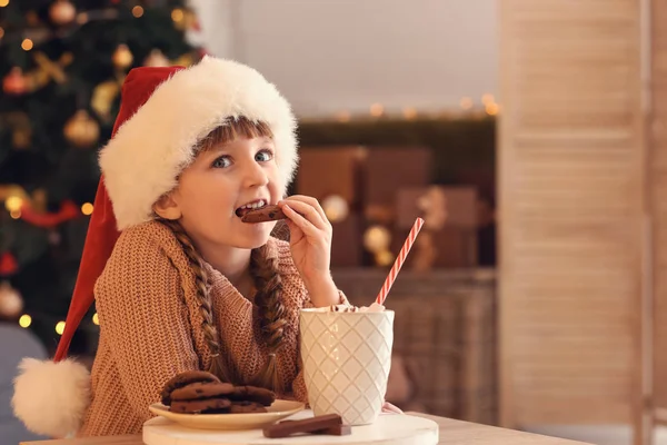 Sıcak çikolata içme ve evde kurabiye yemek Noel arifesinde Noel Baba şapkası, sevimli küçük kız