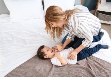 Sevimli küçük oğluyla evde yatakta oynayan genç anne