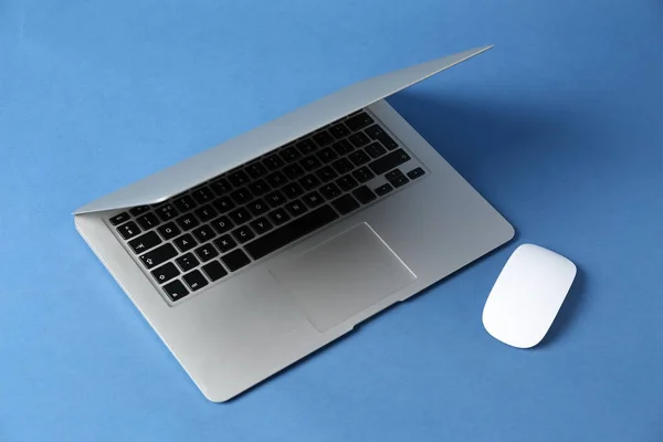 Modern laptop and PC mouse on color background