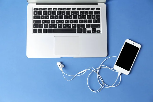 Modern laptop and mobile phone with earphones on color background