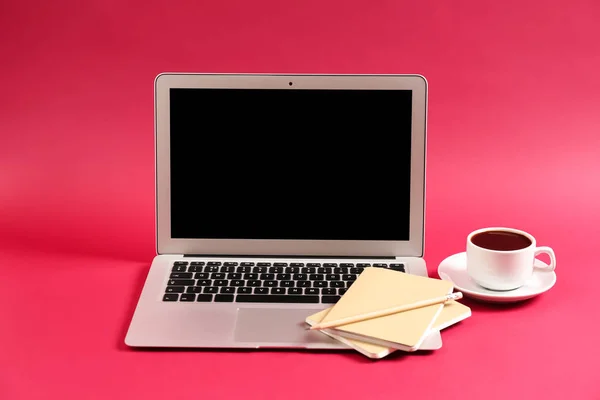 Modern laptop, cup of coffee and notebooks on color background