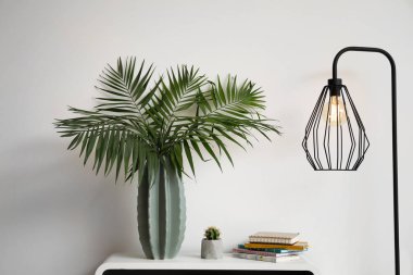 Işık duvarının yakınında tablo vazo ile yeşil tropikal yaprak