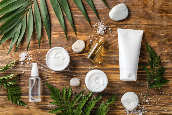 Composition with cosmetic products and tropical leaves on wooden background