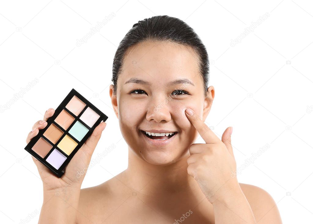 Portrait of young Asian woman with palette of concealers for masking acne on white background