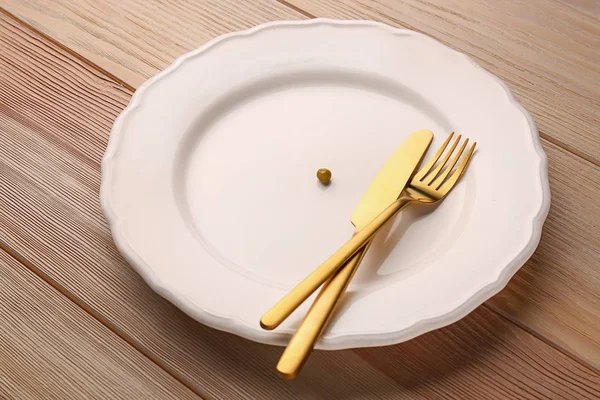 Plate with small peas and cutlery on wooden table. Diet concept