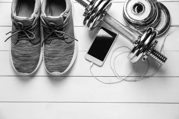 Shoes, sport equipment and mobile phone on white wooden background