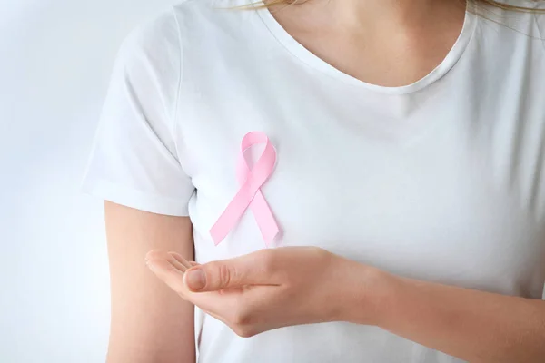 Woman with pink ribbon on white background, closeup. Breast cancer awareness concept