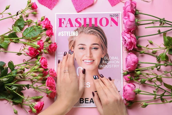 Female hands with fashionable magazine and flowers on color background