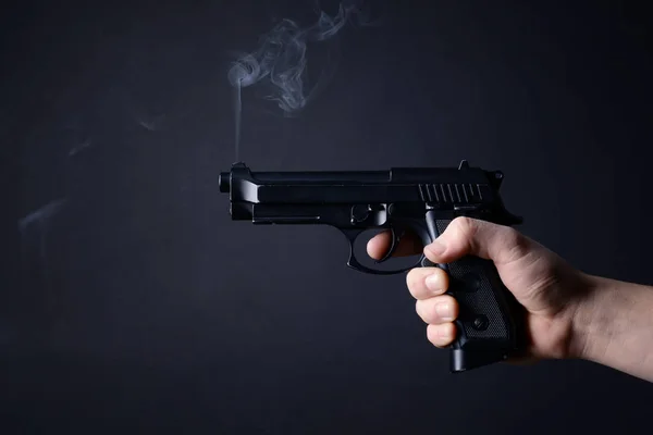 Male hand with smoking gun on dark background