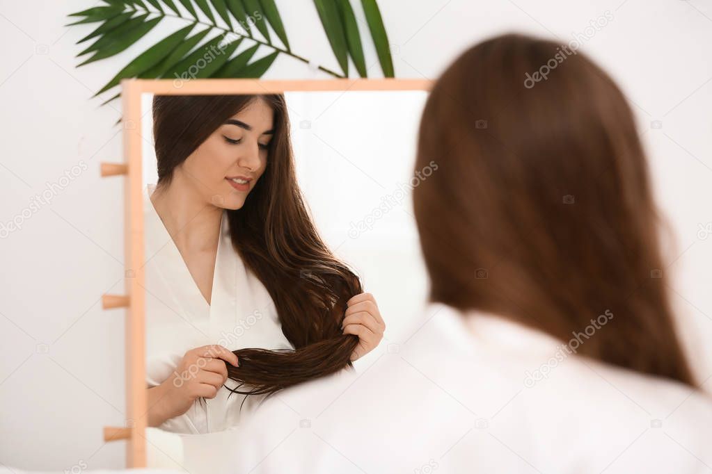 Young woman with beautiful long hair near mirror in bathroom