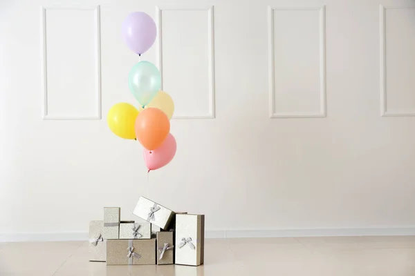 Colorful balloons and gift boxes on floor against light wall