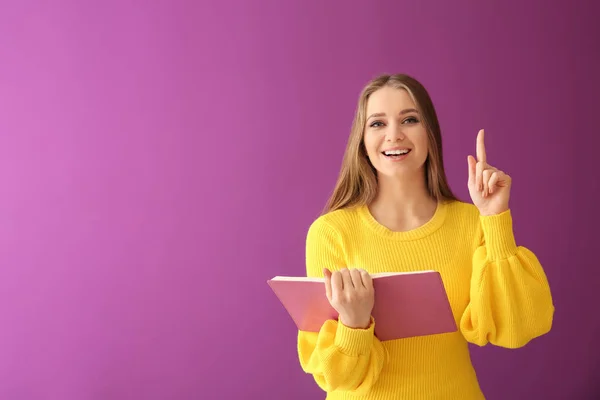 Beautiful young woman with book and raised index finger on color background