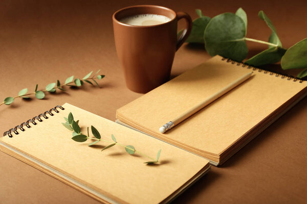 Notebooks, pencil and cup of coffee on color background