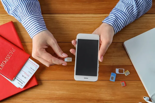 Woman inserting sim card into mobile phone on wooden table