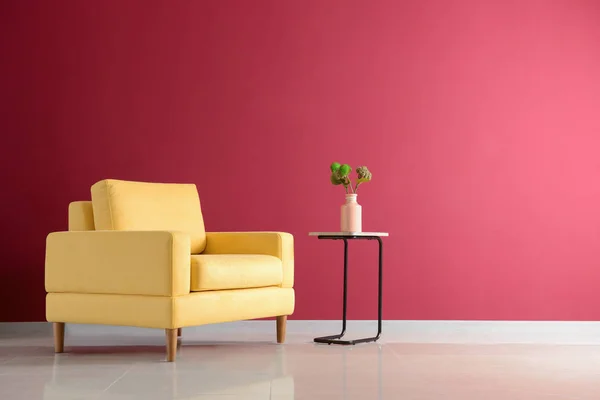 Bright armchair with table near color wall in room