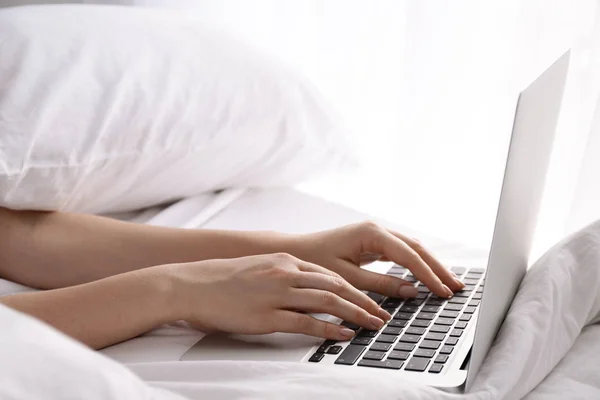 Woman working on laptop in bed, closeup