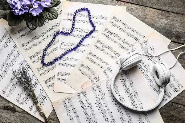 Composition with headphones, flowers and music sheets on wooden table