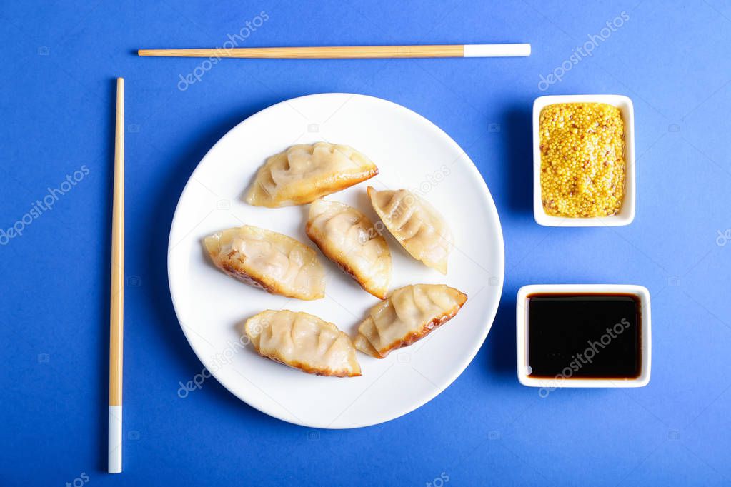 Plate with tasty Japanese gyoza and sauces on color background