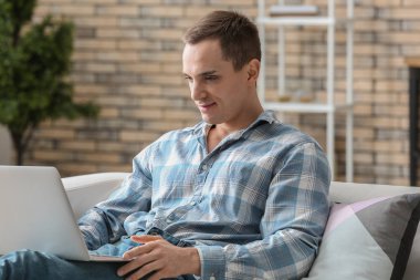 Evde dizüstü bilgisayarda çalışan yakışıklı genç adam.