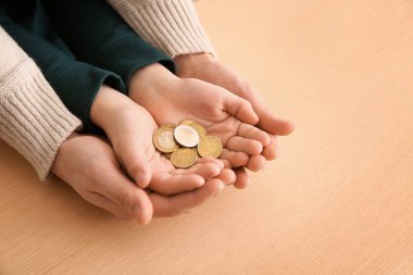 Hands of young man and his son holding coins on wooden table. Concept of child support clipart