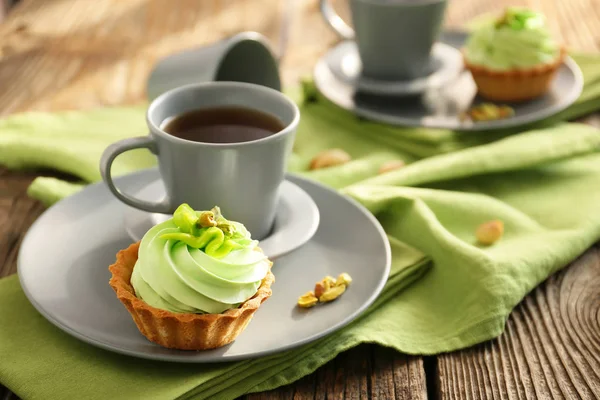 Tasty pistachio tartlet with cup of tea on wooden table