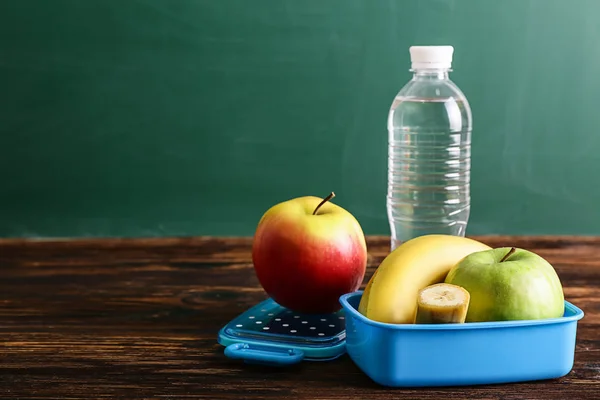 School lunch box with tasty food and bottle of water on table
