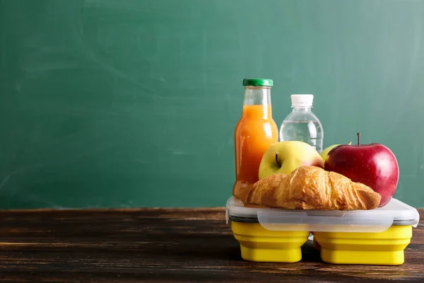 School lunch box with tasty food, bottle with water and juice on table